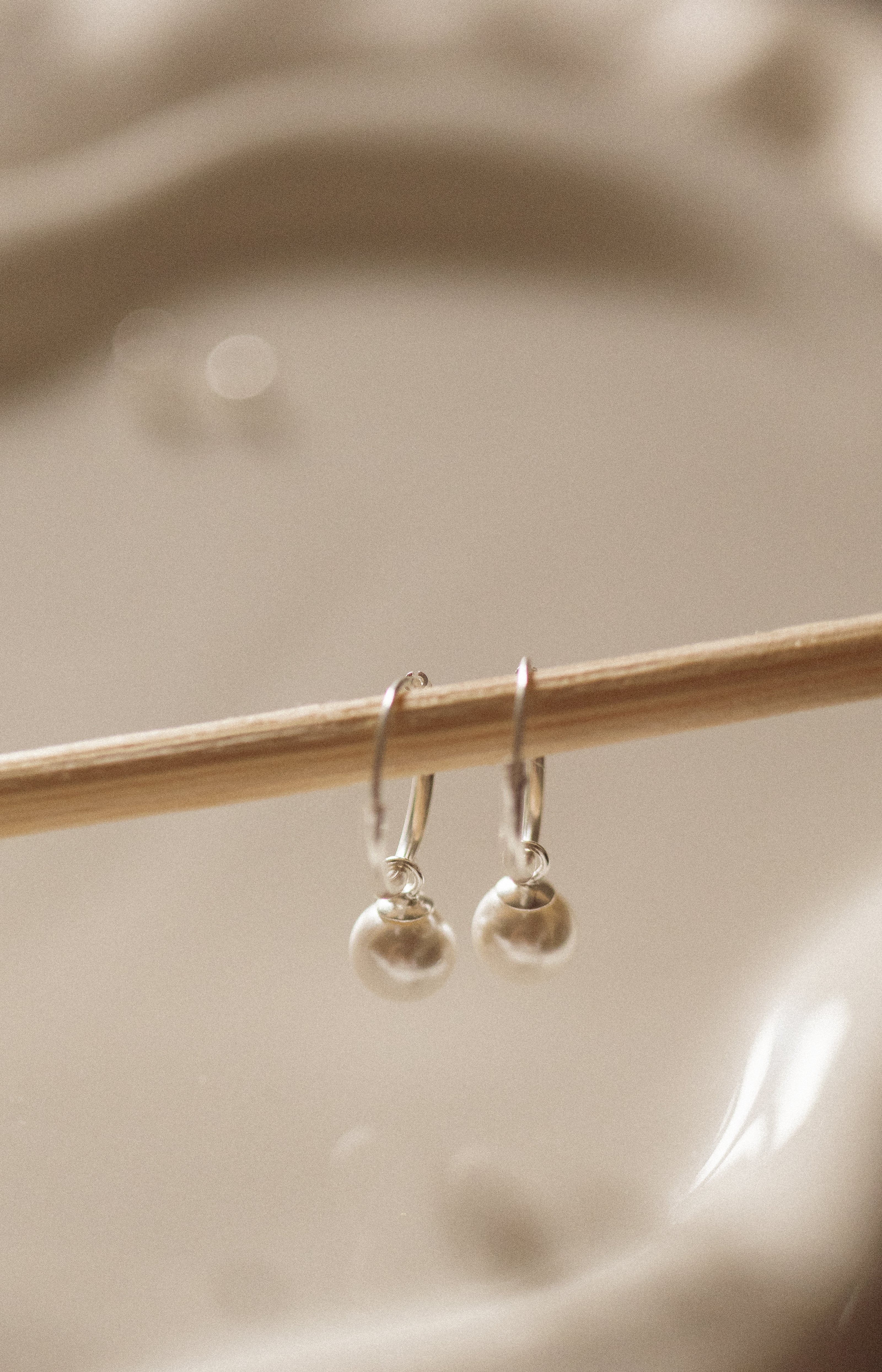 Silver earrings on a wooden stick against a beige background