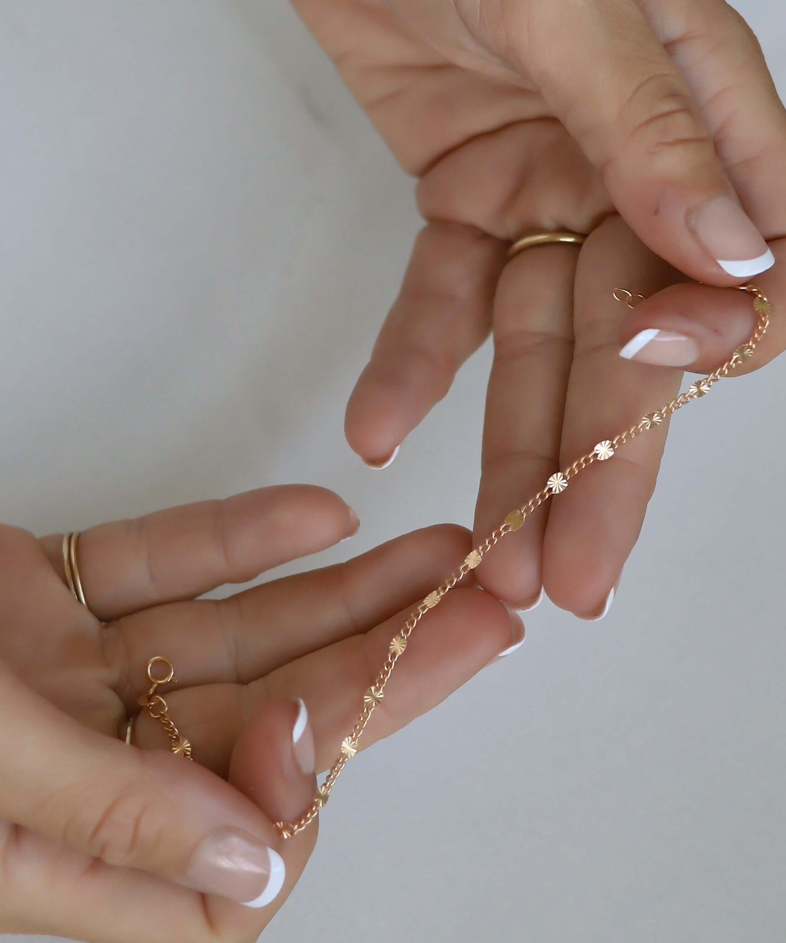 Close-up of hands holding a gold chain necklace against a neutral background