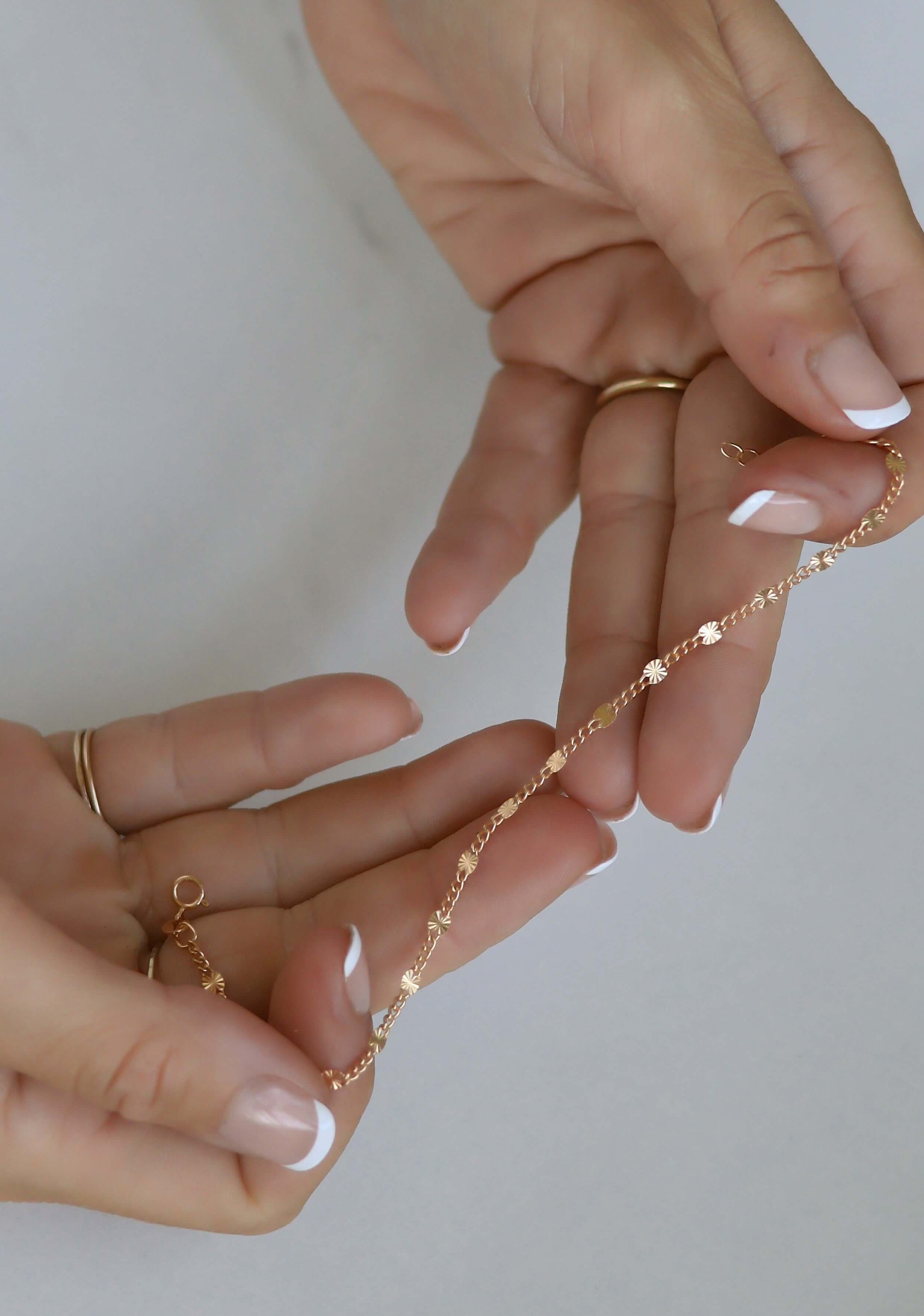Close-up of hands holding a gold chain necklace against a neutral background