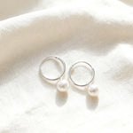 Silver hoop earrings with pearls on a white fabric background