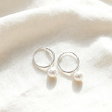 Silver hoop earrings with pearls on a white fabric background
