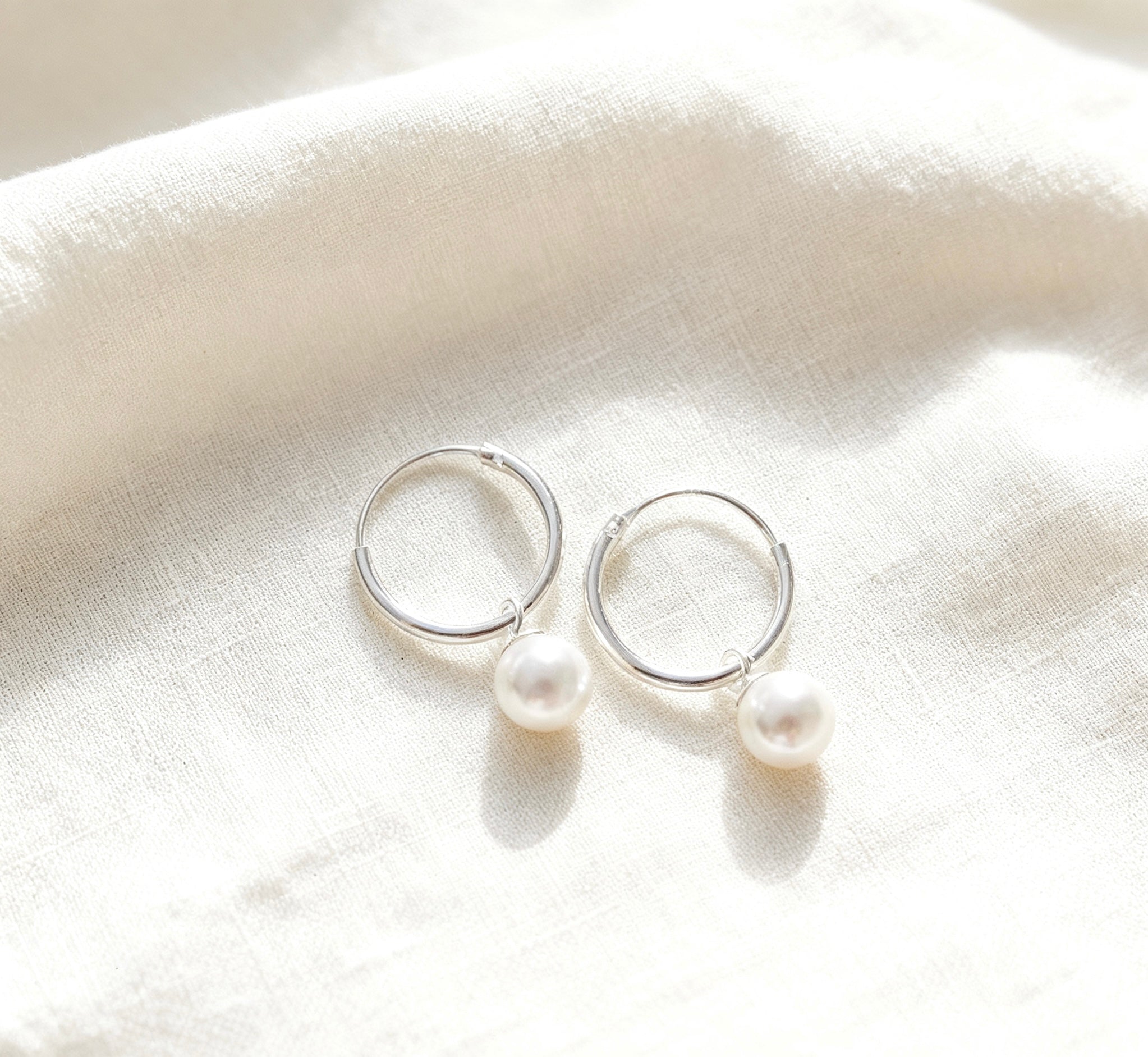 Silver hoop earrings with pearls on a white fabric background