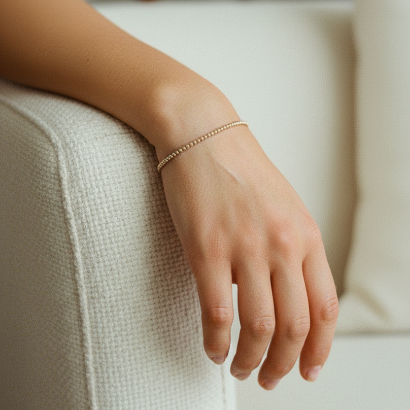 Hand wearing a gold bracelet on a white couch