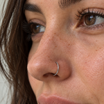 Close-up of a person's face wearing a thin silver-colored curved hoop nose ring.