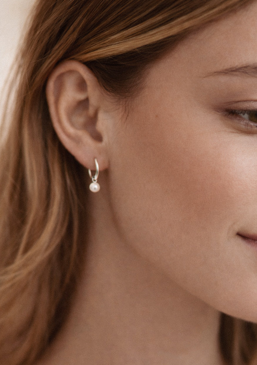 Close-up of a person wearing a pearl earring with a neutral background