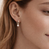 Close-up of a person wearing a pearl earring with a neutral background