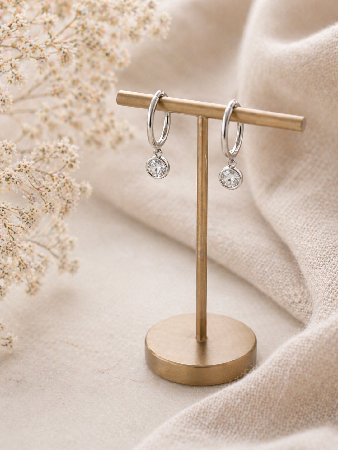 Pair of silver hoop earrings on a gold earring stand with a soft beige background