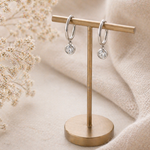 Pair of silver hoop earrings on a gold earring stand with a soft beige background