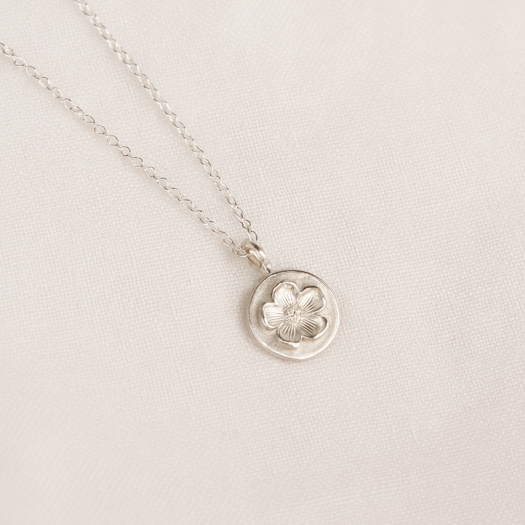 Silver necklace with a floral pendant on a light linen background