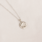 Silver necklace with a floral pendant on a light linen background