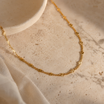 Gold necklace on a textured beige surface with fabric