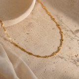 Gold necklace on a textured beige surface with fabric
