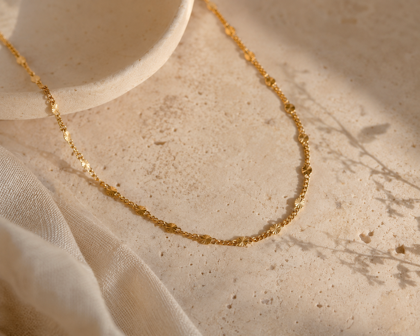 Gold necklace on a textured beige surface with fabric