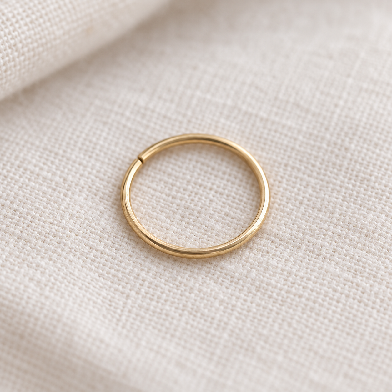 A minimalist gold metal ring, resting on a textured beige linen fabric background.