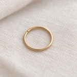 A minimalist gold metal ring, resting on a textured beige linen fabric background.