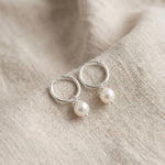 Silver hoop earrings with pearl drops on a beige fabric background