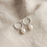 Silver hoop earrings with pearl drops on a beige fabric background