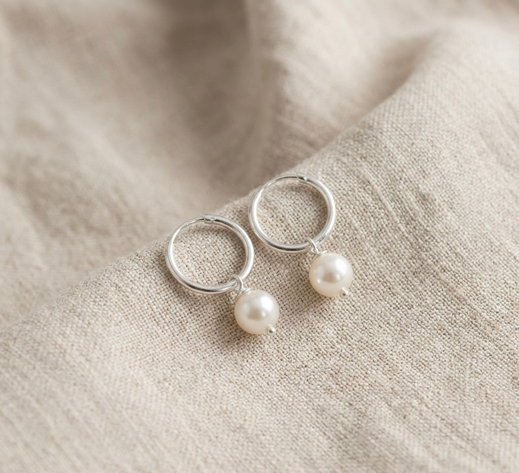 Silver hoop earrings with pearl drops on a beige fabric background