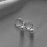 Pair of silver hoop earrings with small pearls on a light gray background