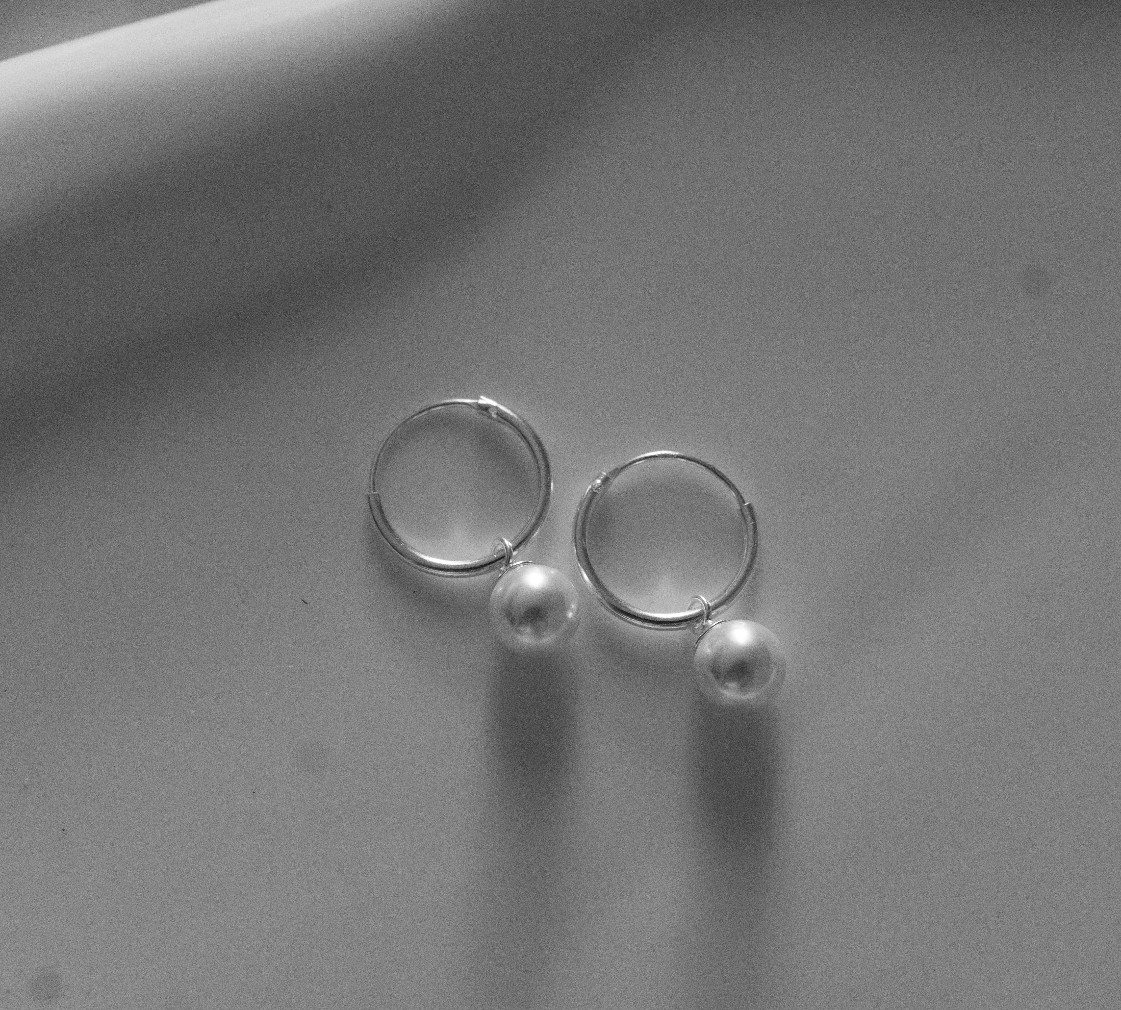 Pair of silver hoop earrings with small pearls on a light gray background