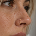 Close-up side profile of a woman wearing a delicate gold crescent moon nose ring.