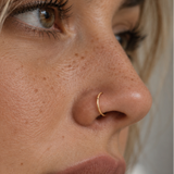 Close-up side profile of a woman wearing a delicate gold crescent moon nose ring.