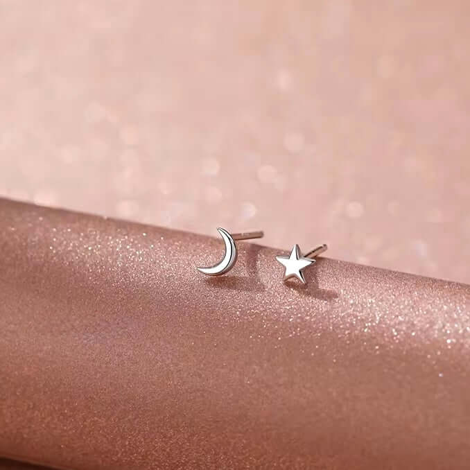 Sterling silver moon and star stud earrings on a soft pink background, perfect for everyday elegance.