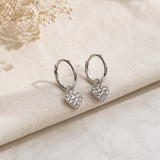 Heart-shaped silver earrings on a soft beige fabric background
