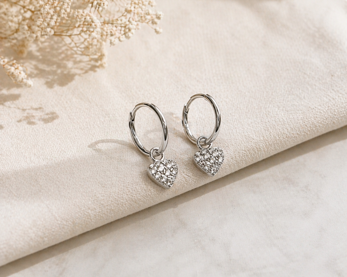 Heart-shaped silver earrings on a soft beige fabric background