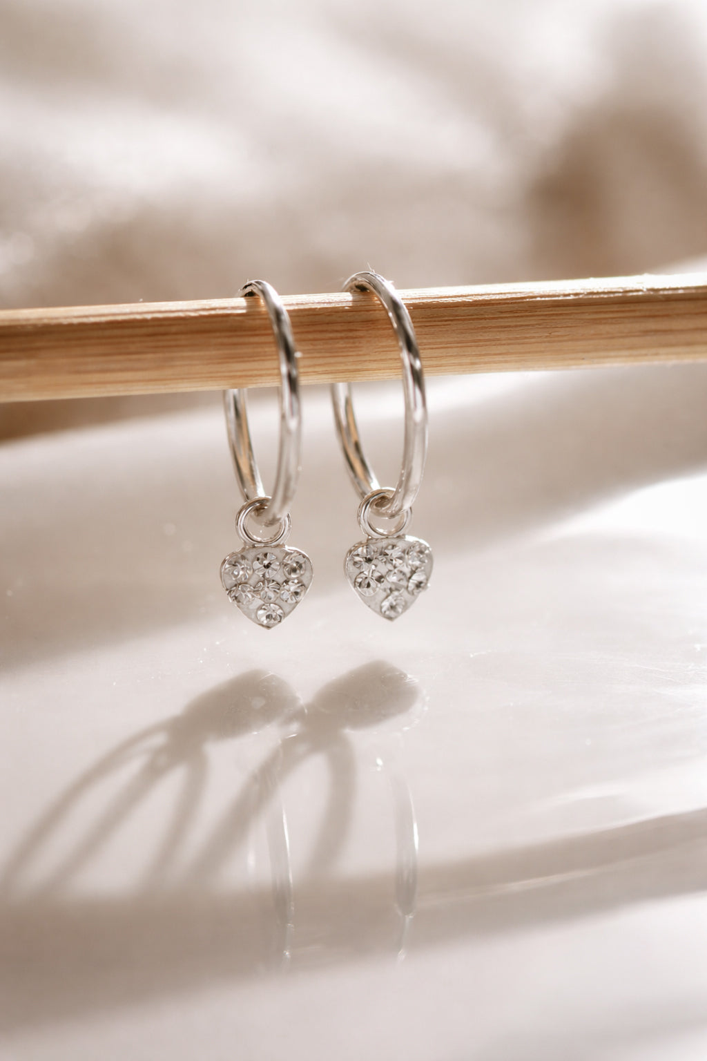 Silver heart-shaped earrings on a wooden stick with a soft background