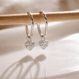 Silver heart-shaped earrings on a wooden stick with a soft background