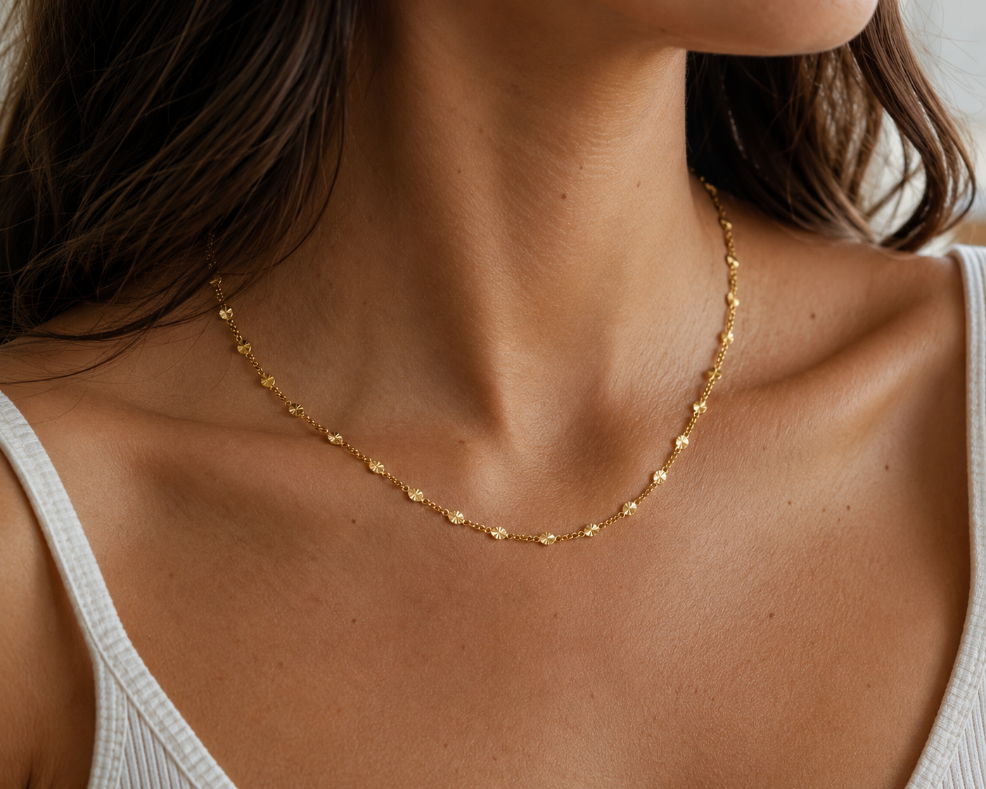 Close-up of a person wearing a gold necklace with a neutral background