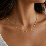 Close-up of a person wearing a gold necklace with a neutral background