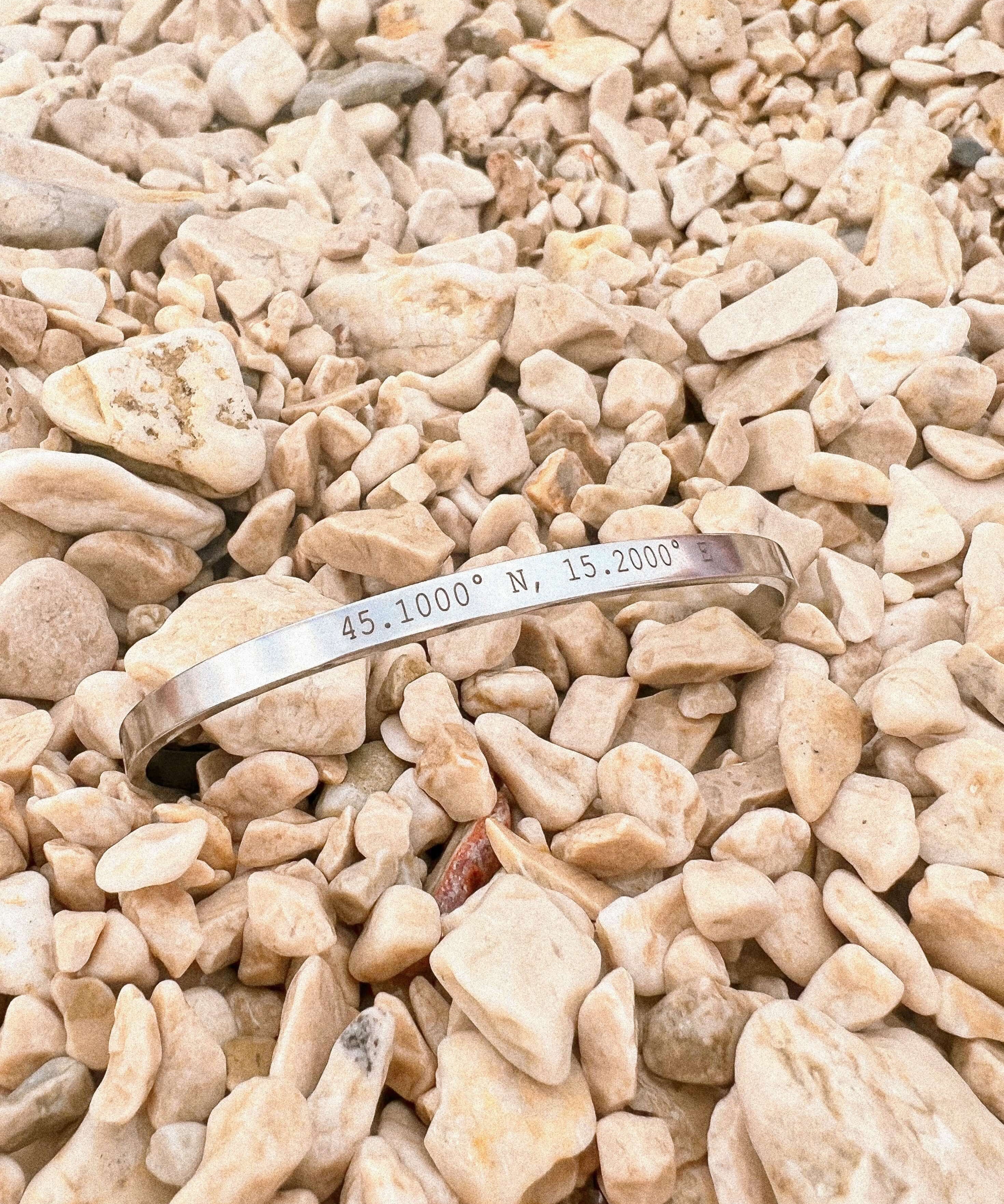 Personalised silver cuff bracelet with coordinates displayed on rocky surface for a meaningful gift.