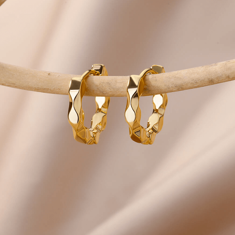 Gold hammered effect huggie hoop earrings displayed on a branch, showcasing elegance and modern style.