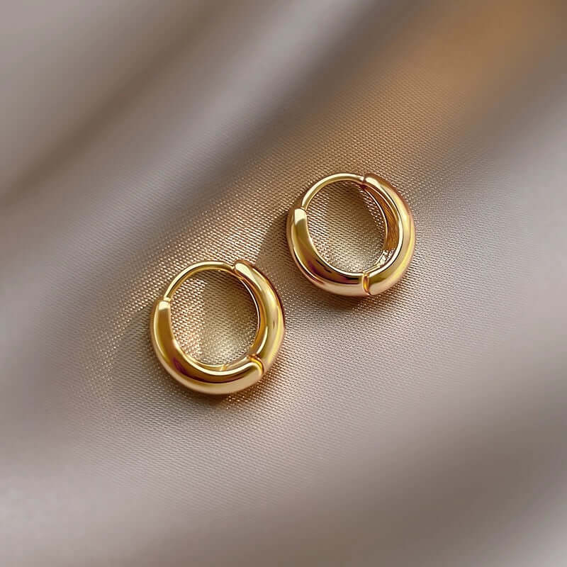 Gold oval hoop earrings on satin fabric, showcasing timeless elegance and sophisticated design.