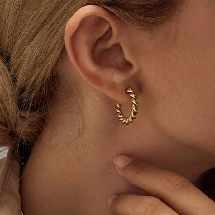 Close-up of a woman wearing twisted gold hoop earrings, showcasing their elegant design and style.