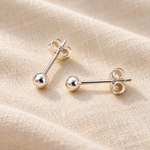 A pair of silver stud earrings with spherical ball studs displayed on a textured beige fabric background.