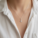 Person wearing a silver necklace with a star pendant against a neutral background