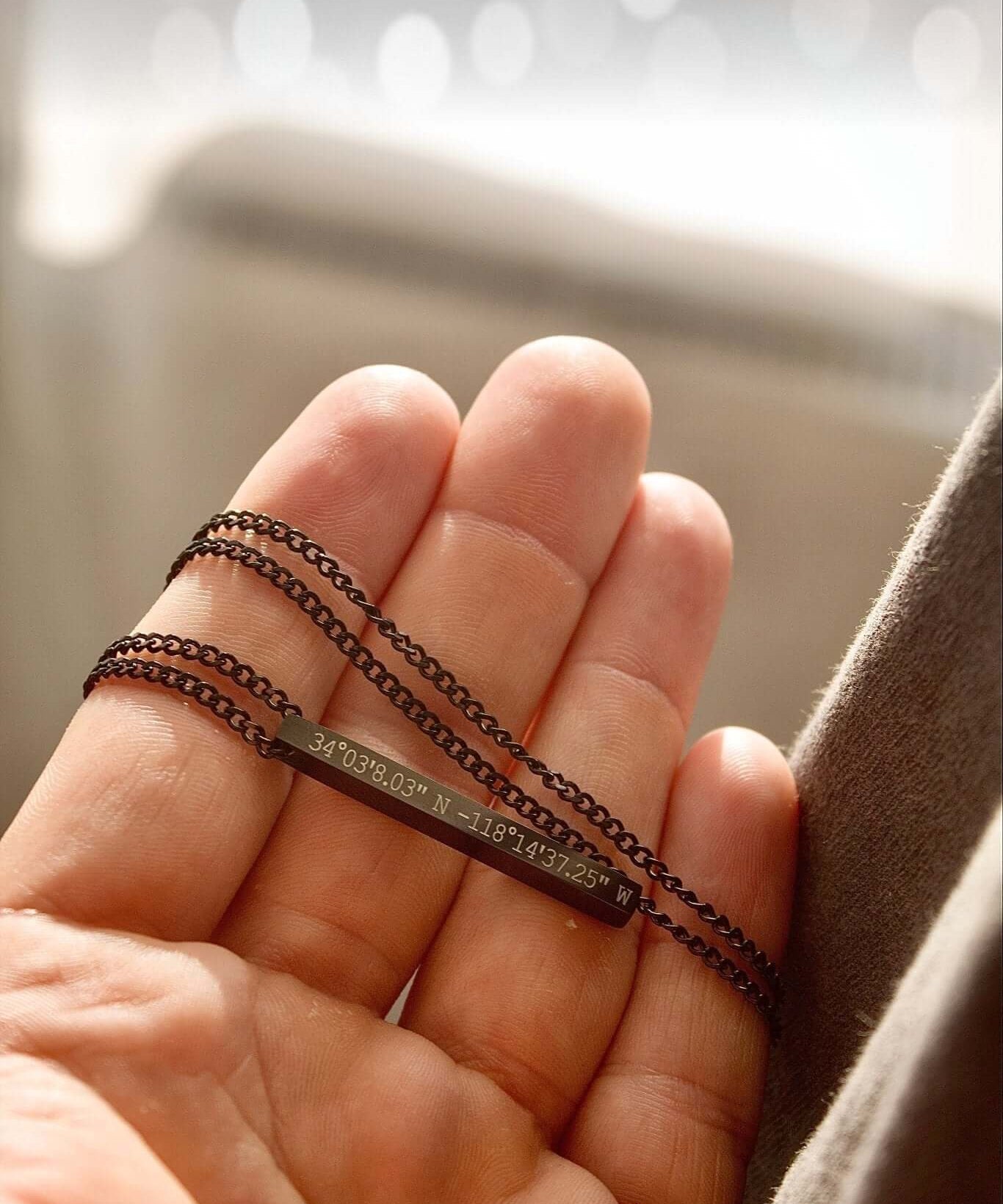 Black personalised bar necklace held in hand, showcasing unique engraving and elegant design.
