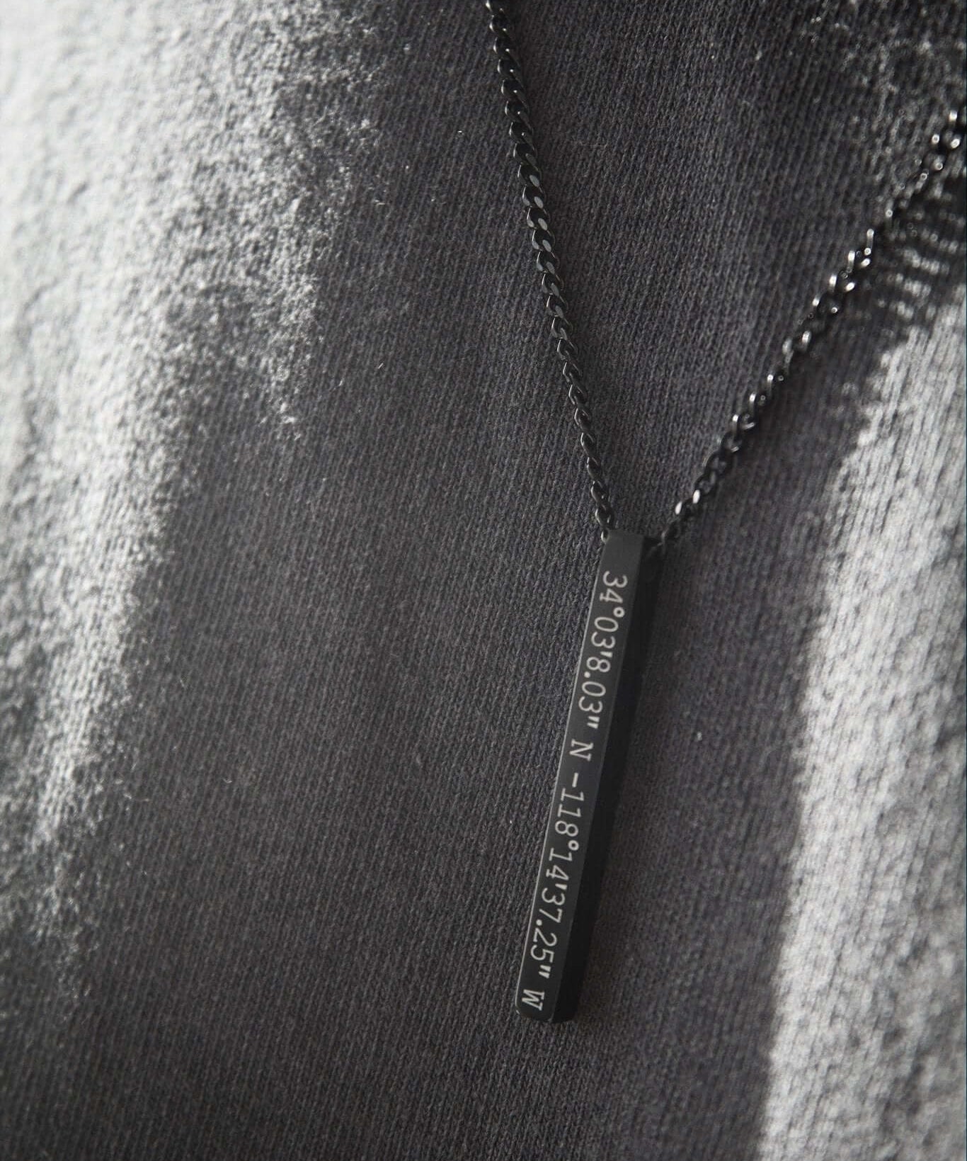 Black personalised bar necklace with engraved coordinates on a grey background, showcasing elegance and meaning.