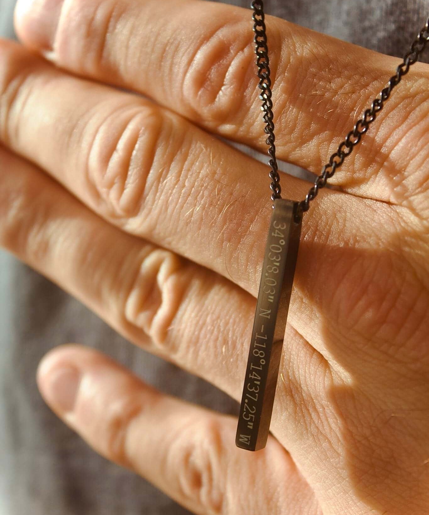 Black personalised bar necklace being held, showcasing its elegant design and potential for custom engraving.