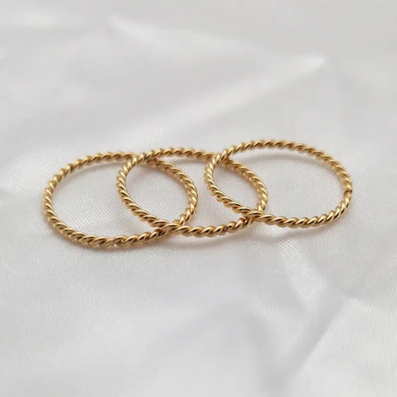 Three gold twisted stacking rings arranged elegantly on soft fabric.