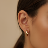 Gold hoop earrings worn by a model against a neutral background