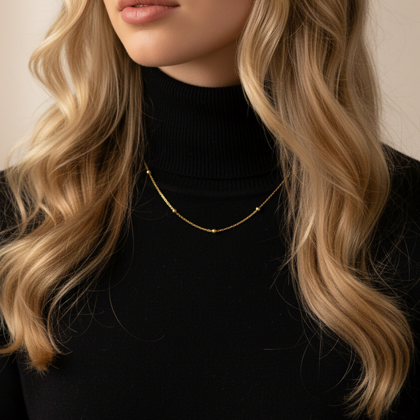 Woman wearing a black turtleneck and gold necklace with wavy blonde hair.