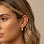 Close-up of a woman wearing gold hoop earrings with a neutral background