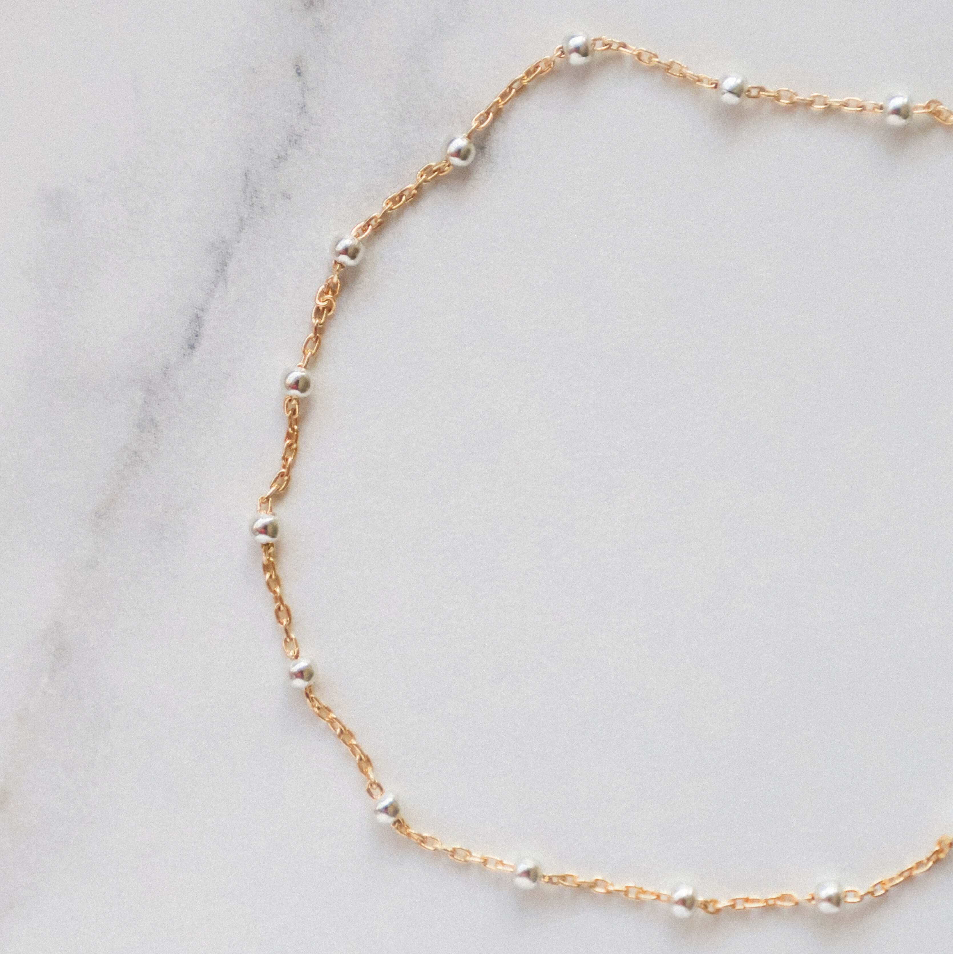 Gold satellite bracelet with sterling silver beads on a marble background.