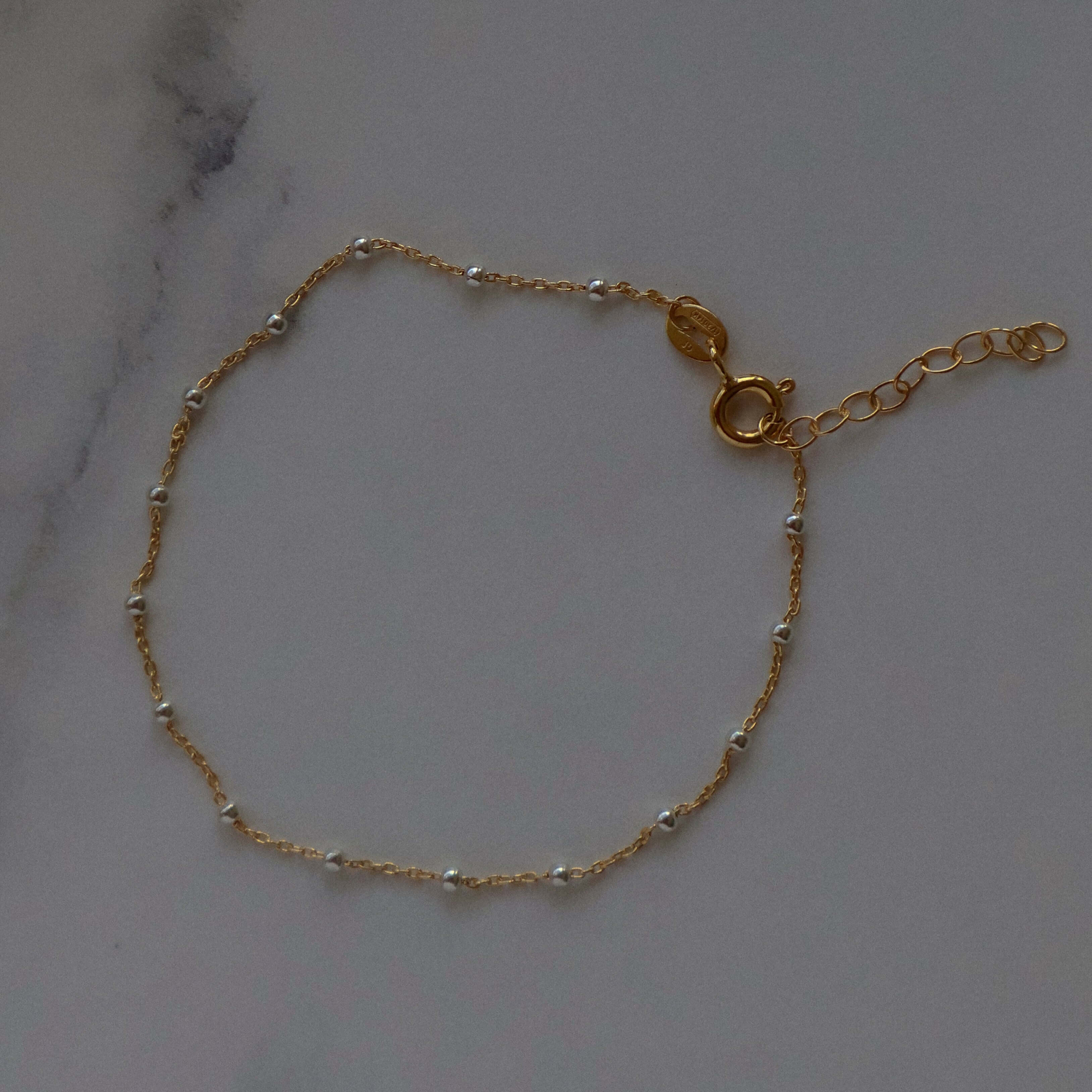 14k Gold Satellite Bracelet with Sterling Silver Beads on marble surface, handmade and adjustable for a perfect fit.
