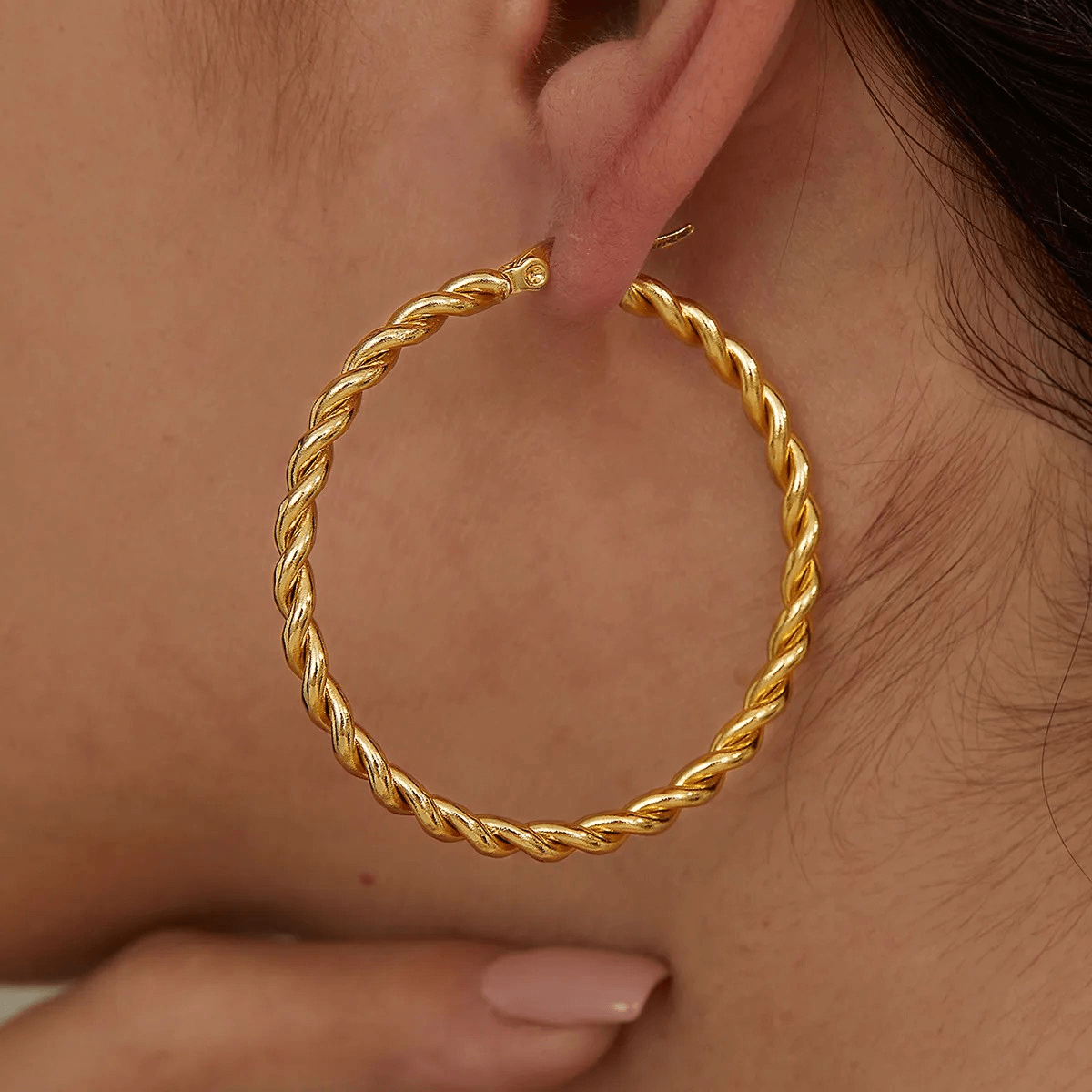 Big gold twisted hoop earrings on a person, showcasing an elegant design perfect for any occasion.