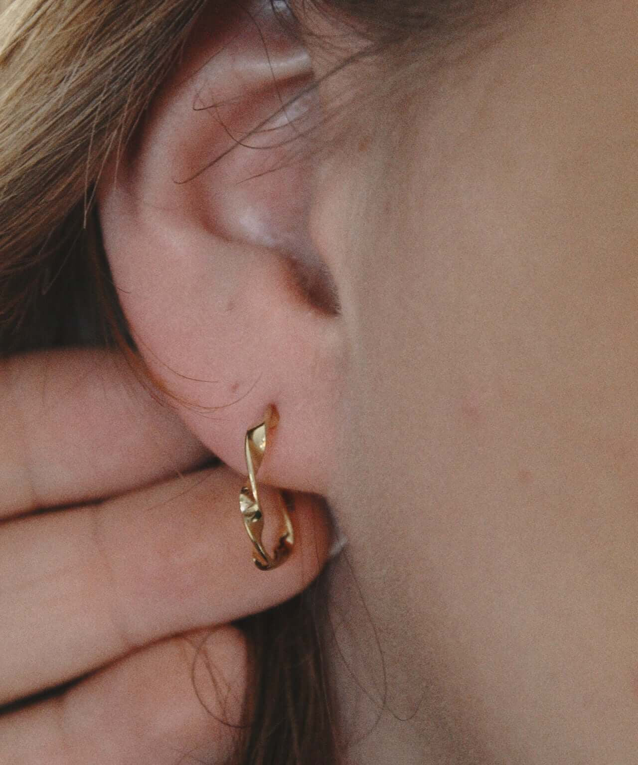 Gold twisted hoop earrings showcased on a model's ear, highlighting their elegant design and secure fit.
